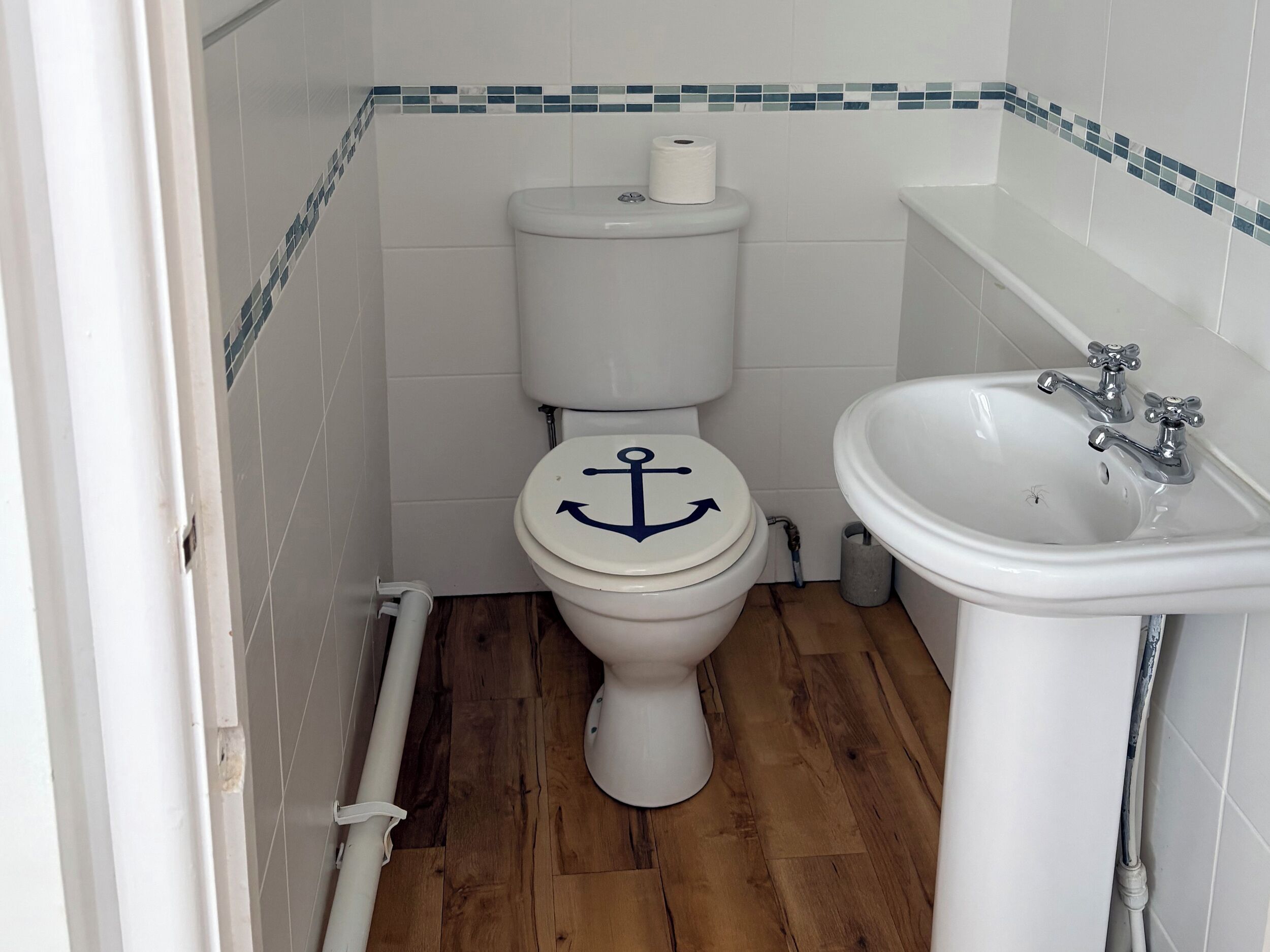 A bathroom with a toilet, a sink, and wooden flooring.