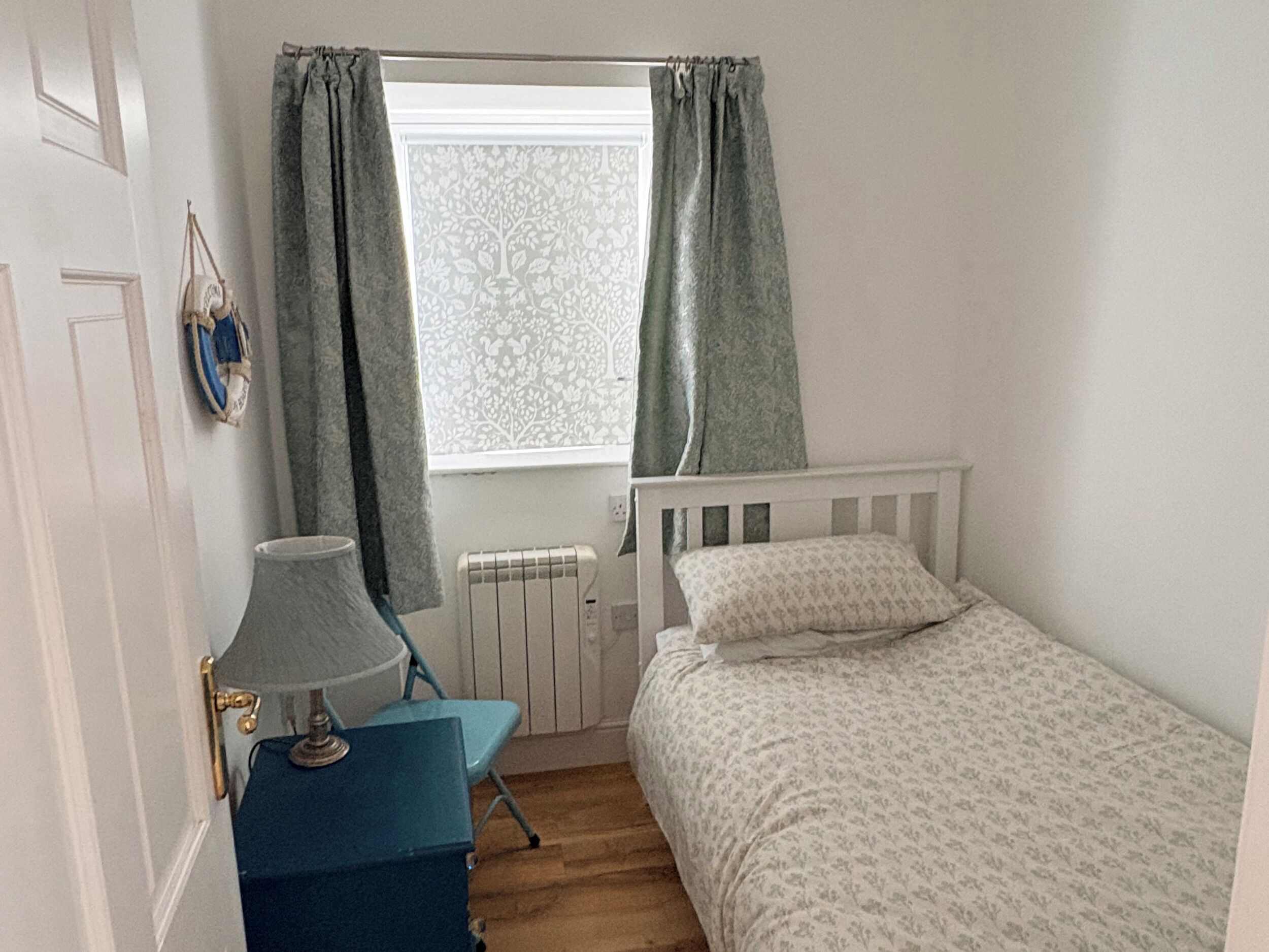 A bedroom with a window, a radiator, a bed, a chair, and a lamp.