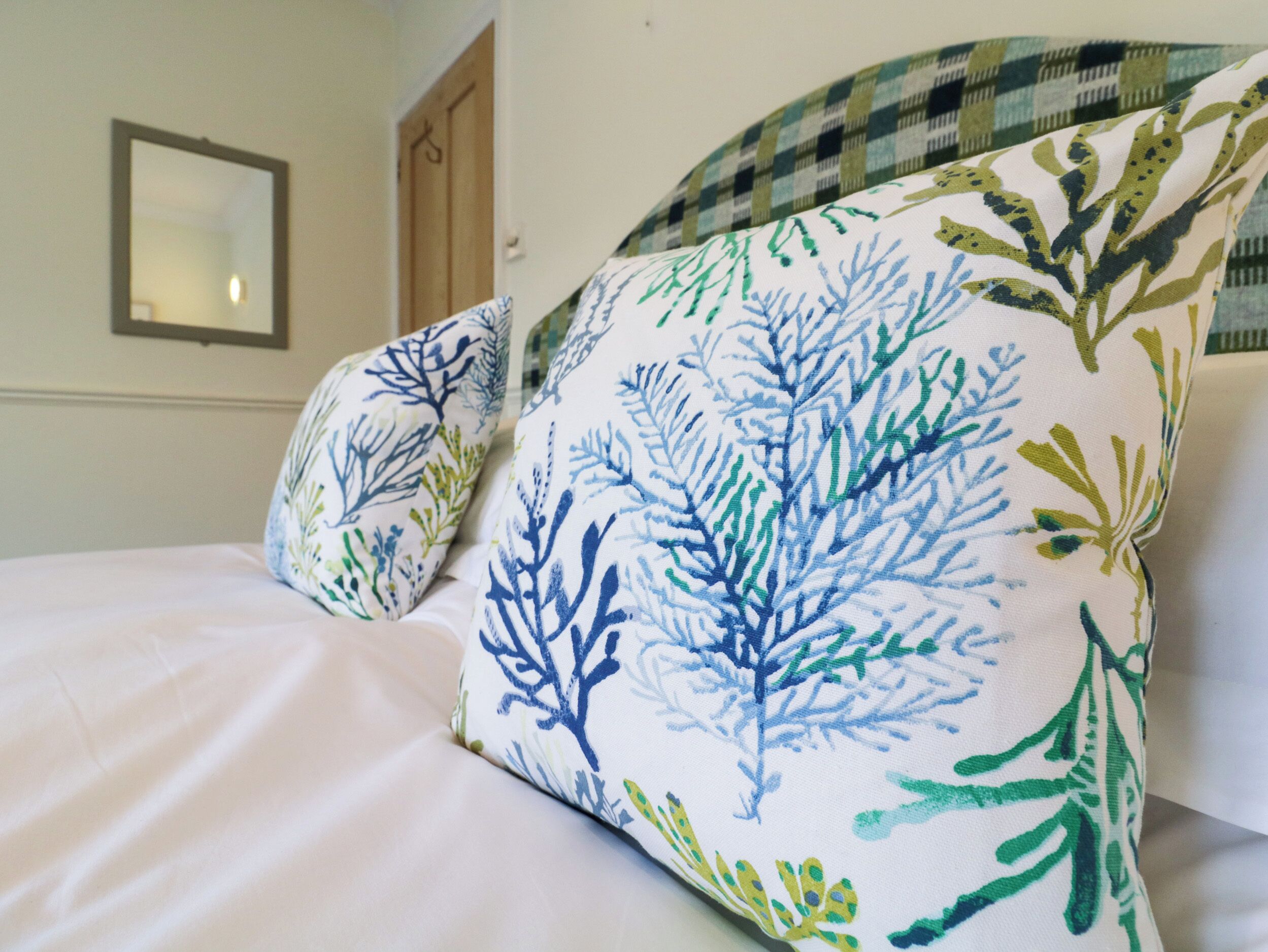 Un lit avec une literie blanche et deux oreillers ornés d’un motif de feuilles bleues et vertes.