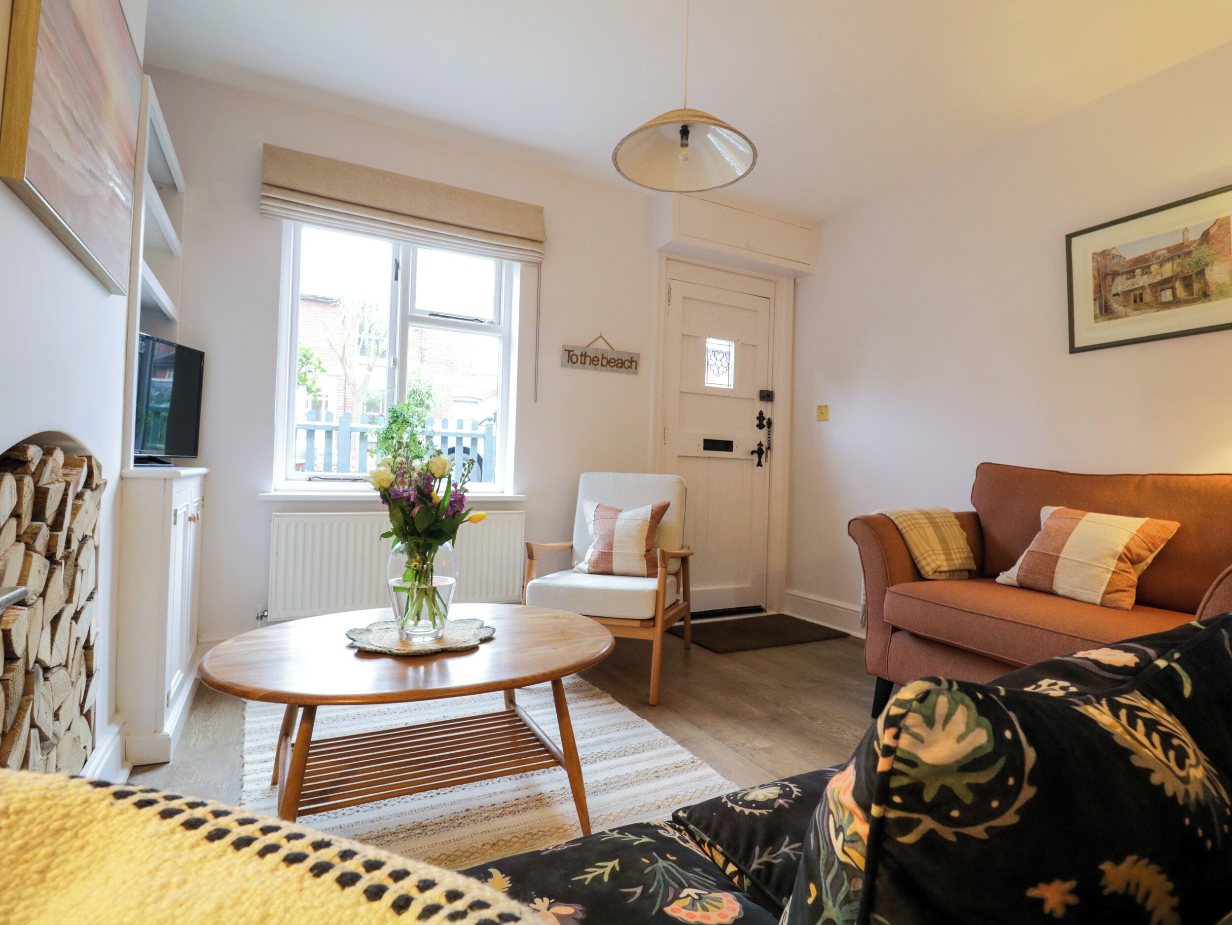 A living room with a round wooden coffee table, a white armchair, a sofa with patterned cushions, and a television on the wall.