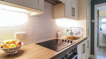 A modern kitchen with a wooden countertop, a built-in stove, and a bowl of fruit.