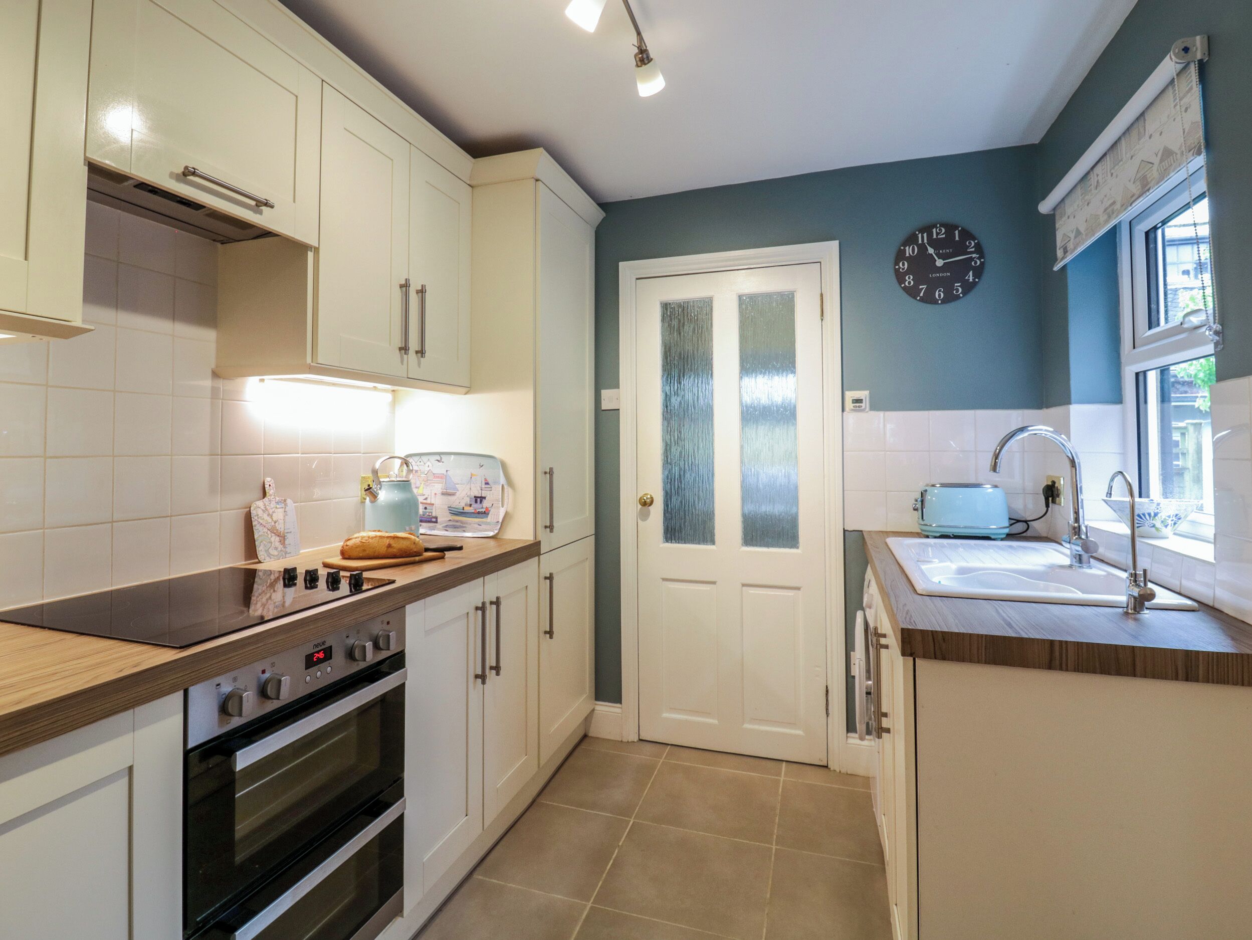 A kitchen with white cabinets, a stove, a toaster, and a clock on the wall.