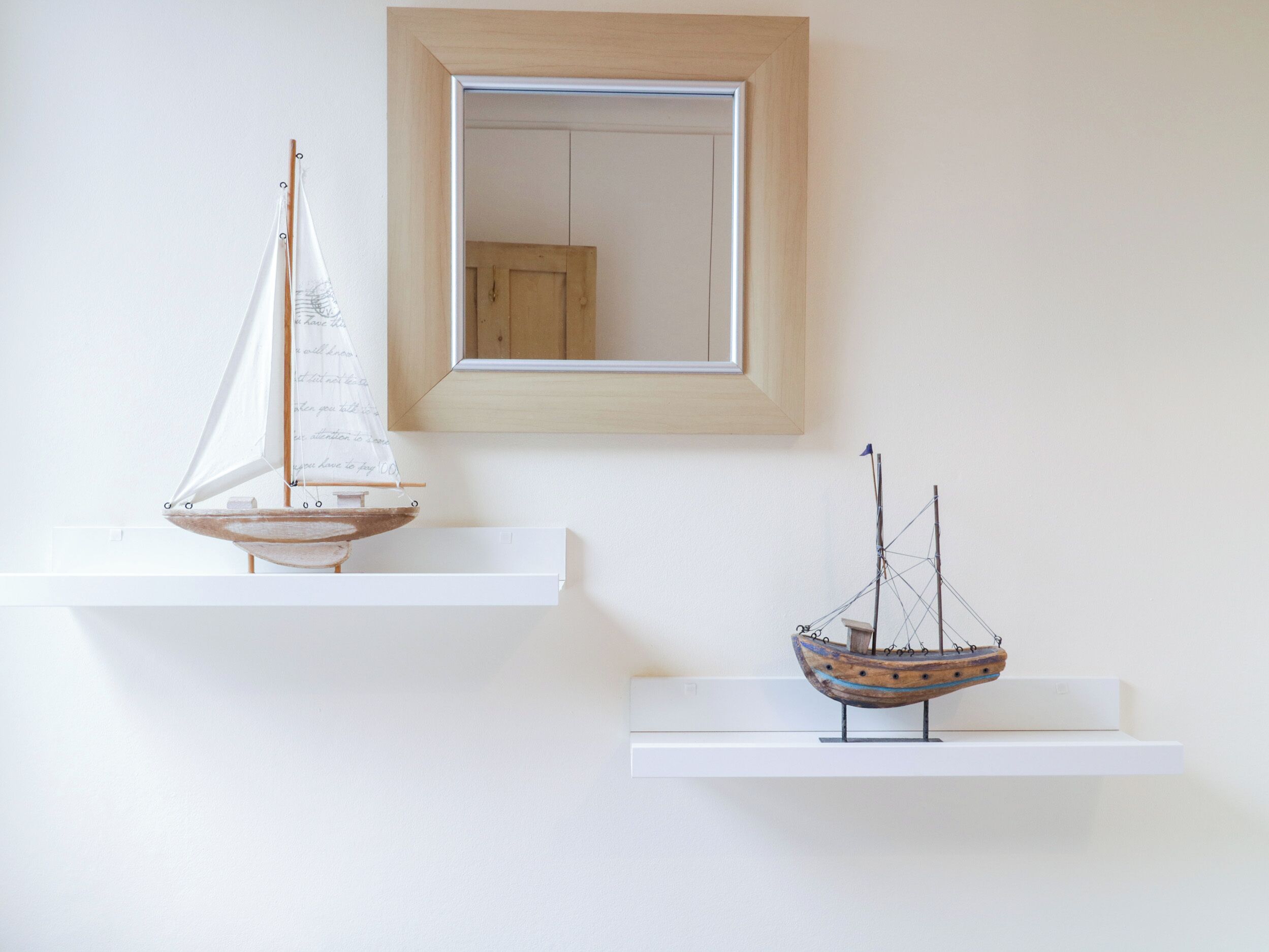 Two wooden model ships on white shelves against a plain wall.