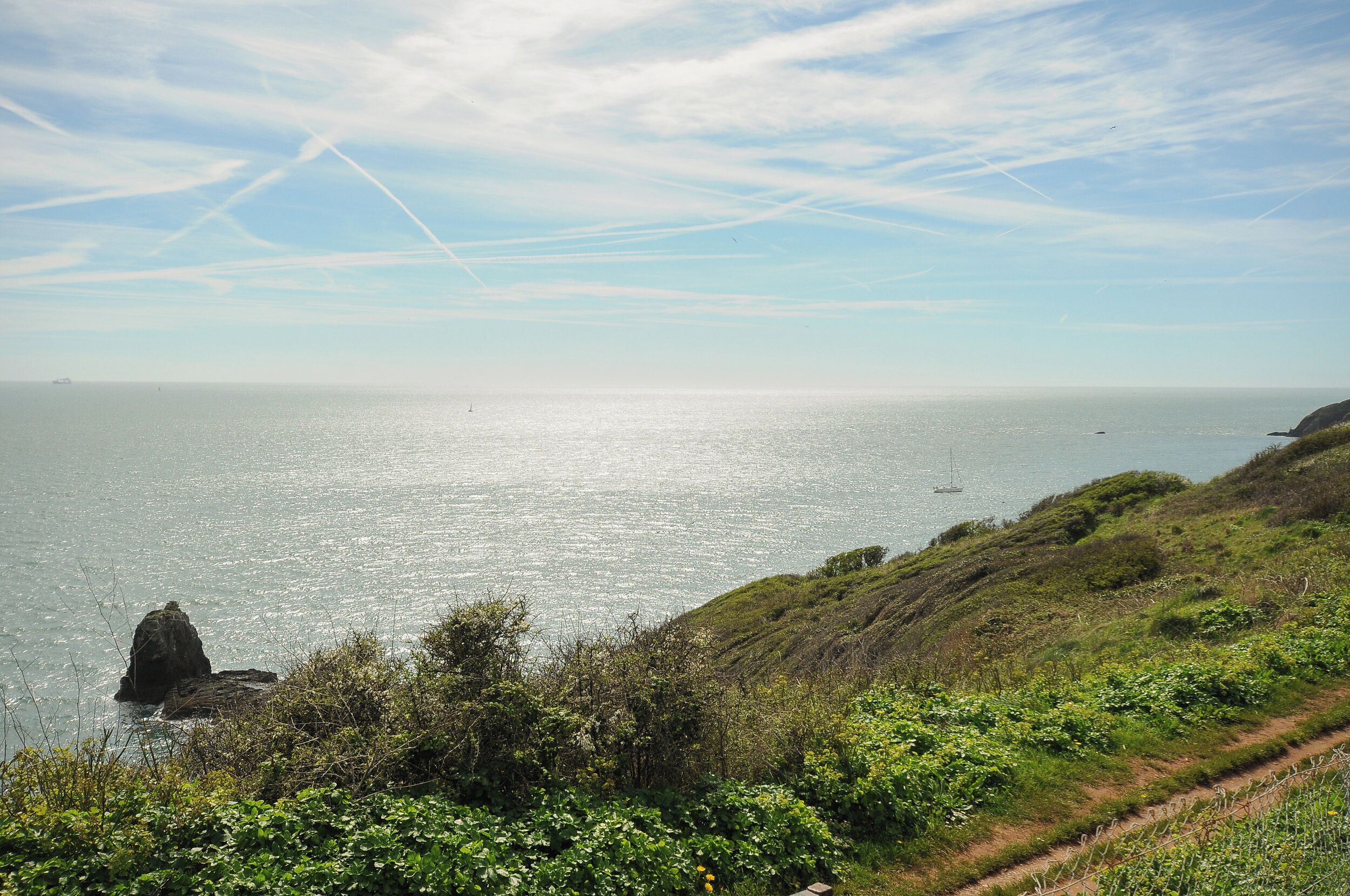 Un paysage côtier avec un ciel dégagé, un affleurement rocheux et un sentier qui mène à la mer.