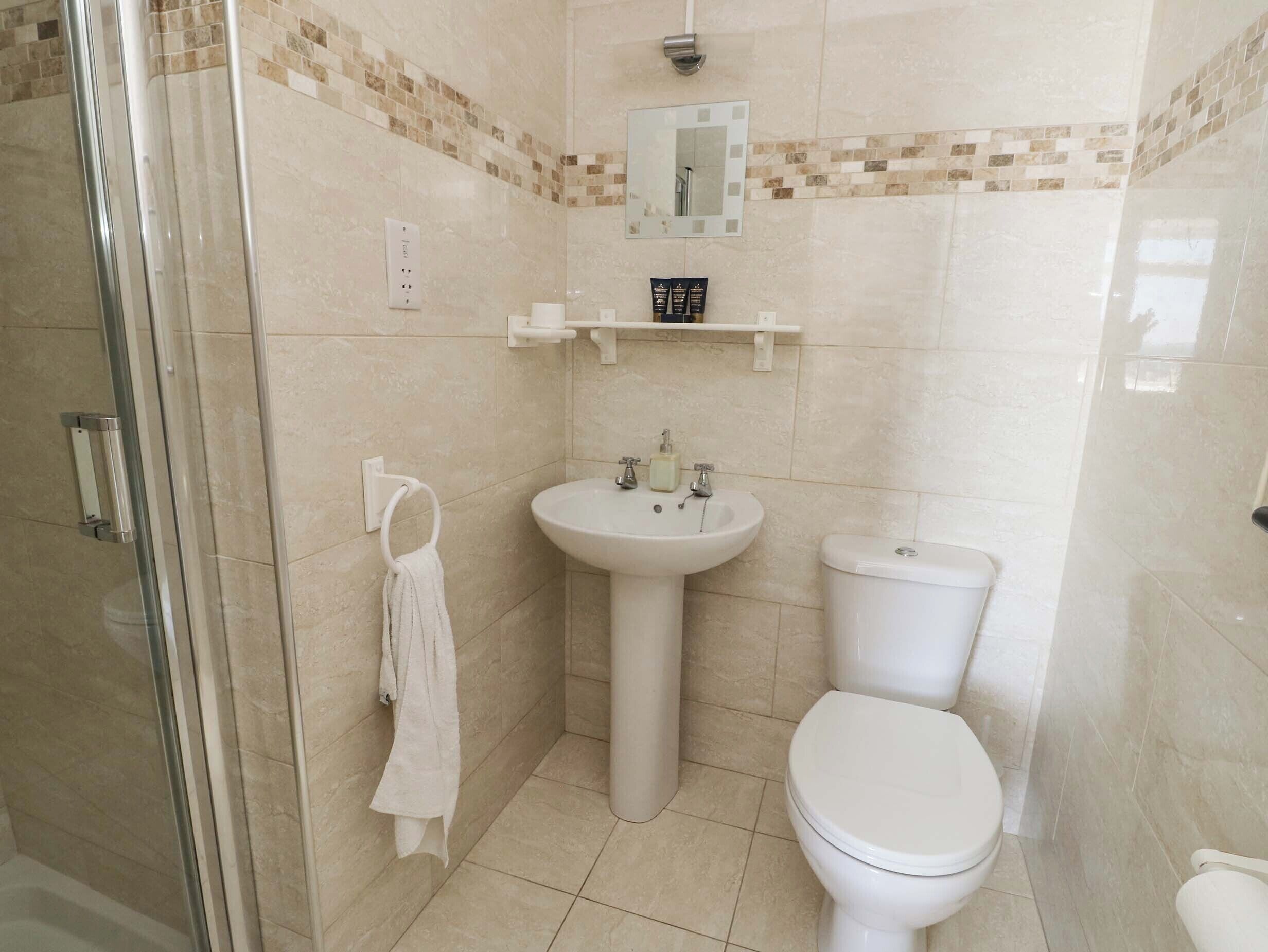 Un baño con cabina de ducha de vidrio, lavabo pedestal, inodoro y espejo sobre el lavabo.