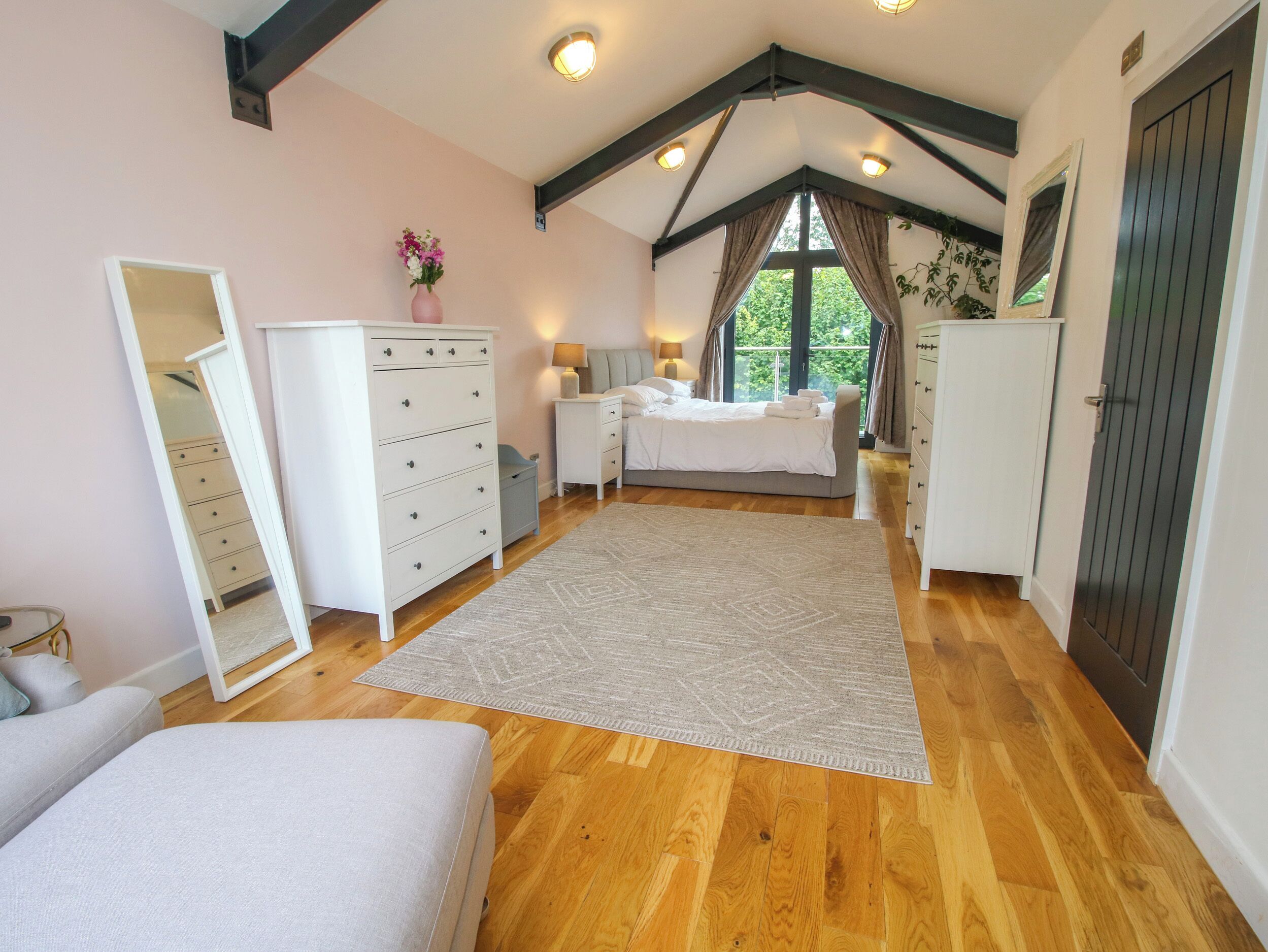 Une chambre à coucher avec un lit, une commode, un miroir et une fenêtre avec des rideaux.