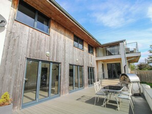 A modern house with a wooden facade, large sliding glass doors, a deck with outdoor furniture, and a second-story balcony. - Timberdyne (Ludlow)