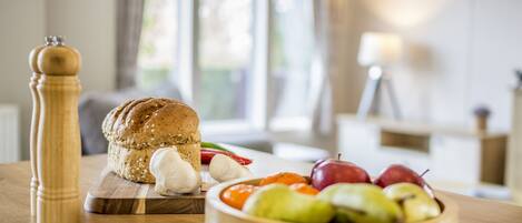 A wooden table with a loaf of bread, a bowl of fruit, and a pepper grinder.