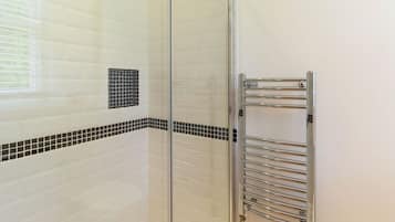 A glass-enclosed shower with white tiles and black accents, a chrome towel rack, and a window with blinds.