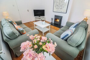 A living room with a sofa, a coffee table, a flat-screen TV, a fireplace, and a framed artwork on the wall. - Bod A Quinte (St Ives)