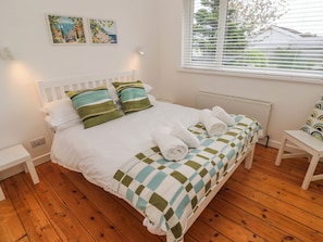 A neatly made bed with pillows, a white headboard, and a view of the outdoors through a window with blinds.
