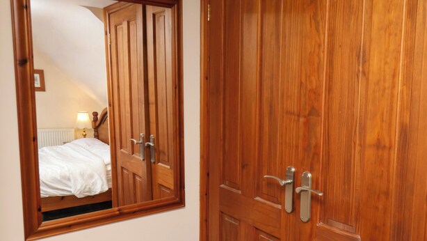 Una puerta de madera con un espejo que refleja una cama y una lámpara.