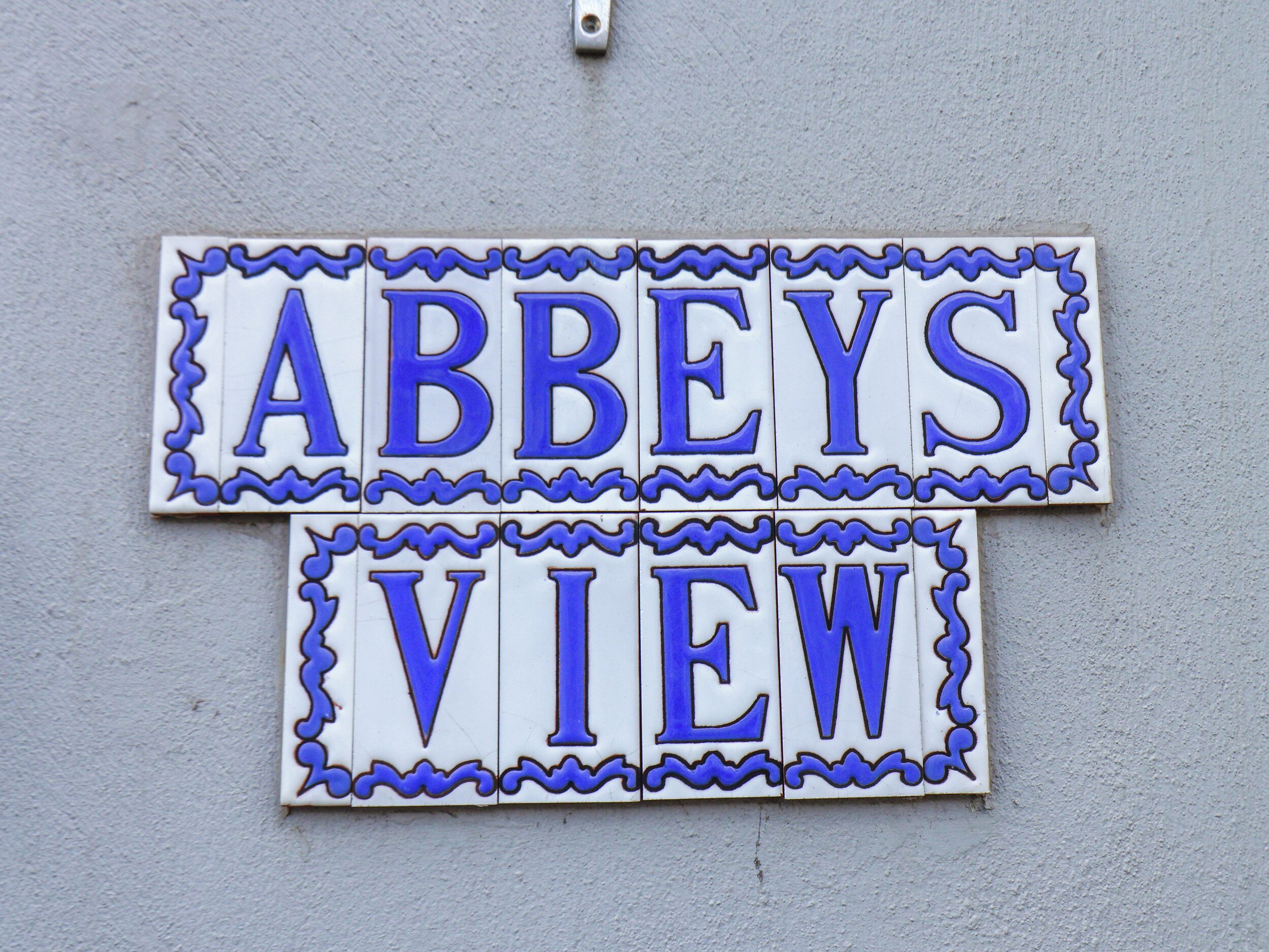 Twee rechthoekige borden met blauwe letters op een lichtgrijze muur.