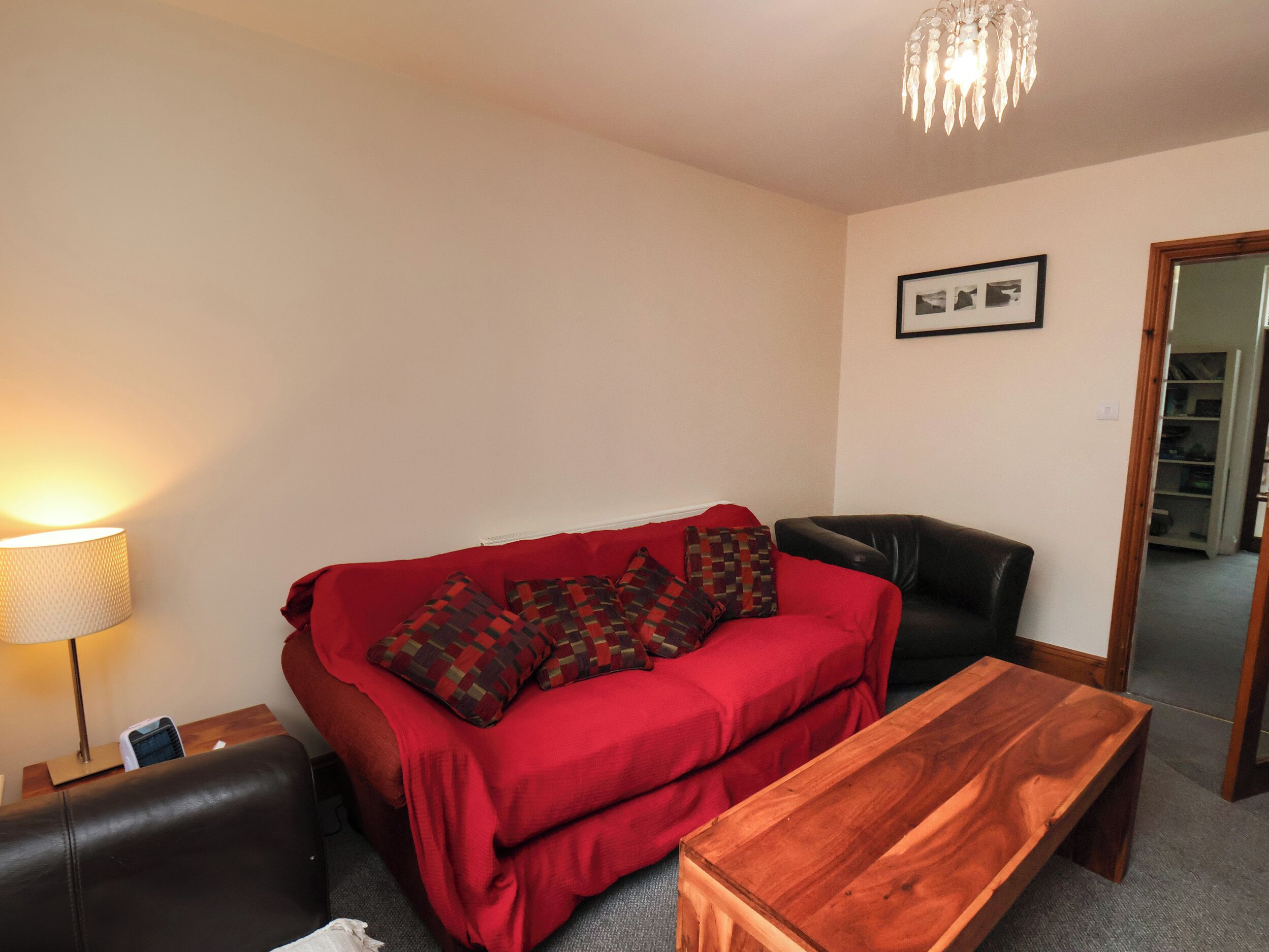 A living room with a red sofa, a wooden coffee table, a black leather chair, a lamp, and a chandelier.