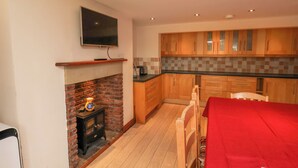 Una cocina con gabinetes de madera, salpicadero de azulejos, estufa integrada y un televisor de pantalla plana montado sobre la chimenea.
