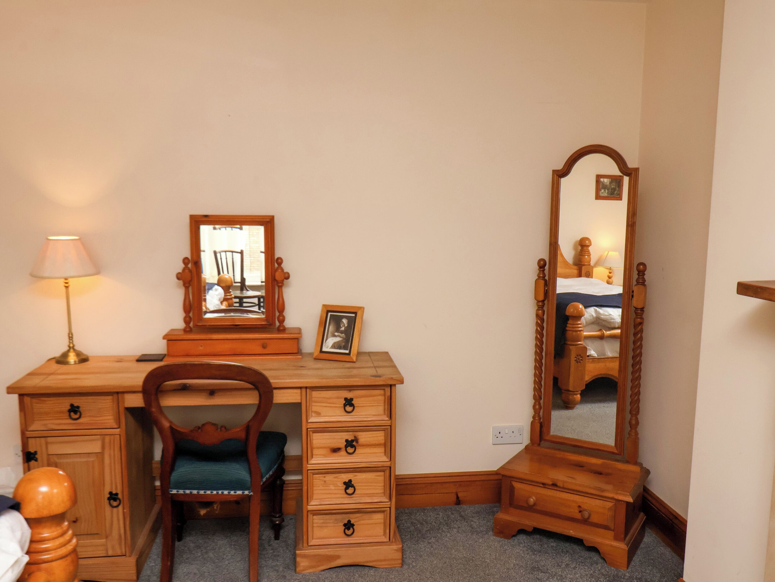 Un bureau en bois, une chaise, un miroir, une lampe et une commode.