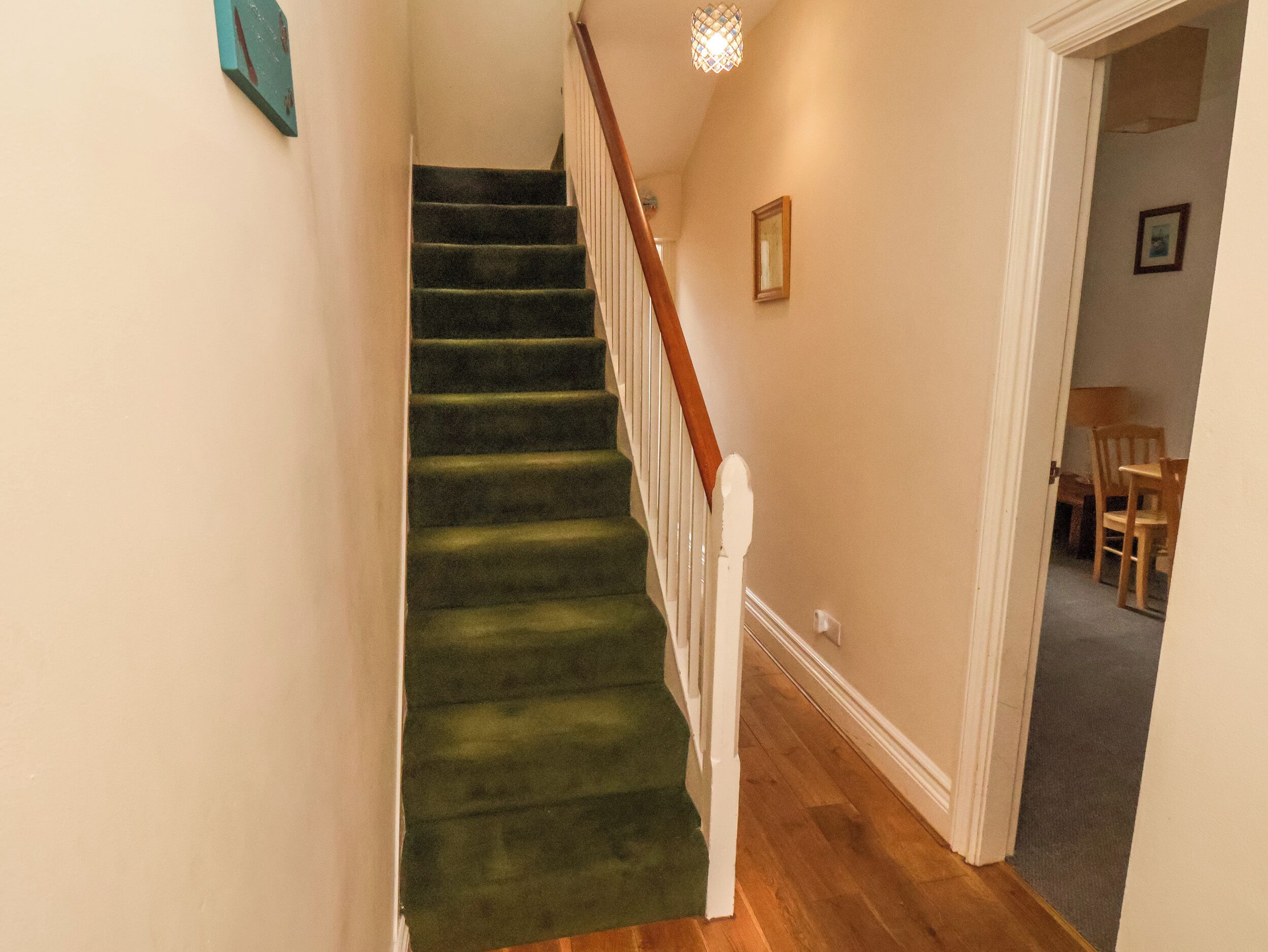 A staircase with green carpet and white railings, leading to a room with a wooden floor and a door leading to another room.