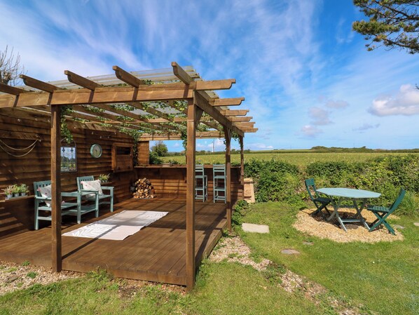 A wooden pergola with a wooden deck, outdoor seating, and a view of the countryside.