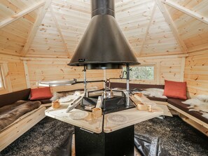 A wooden cabin interior with a central stove, seating area, and a window. - 1 Gilpin House (Kendal)