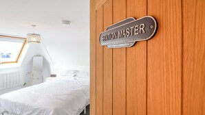 A bedroom with a bed, a wooden door with a sign reading "STATION MASTER", a window with a view, and a radiator. - The Railway Cottage (Llandudno)