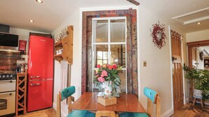 A kitchen with a red refrigerator, wooden chairs, a wooden table, and a window with a view of the outside. - The Bike Shed (Romsey)