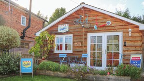 A wooden building with a sign for 'Wall's Ice Cream' and a 'The Bike Shed' sign. There are blue chairs outside and a sign for 'Lyon's Maid Ice Cream'. - The Bike Shed (Romsey)