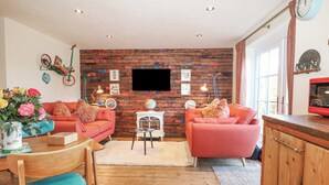 A cozy living room with a brick wall, two sofas, a coffee table, and a TV mounted on the wall. - The Bike Shed (Romsey)