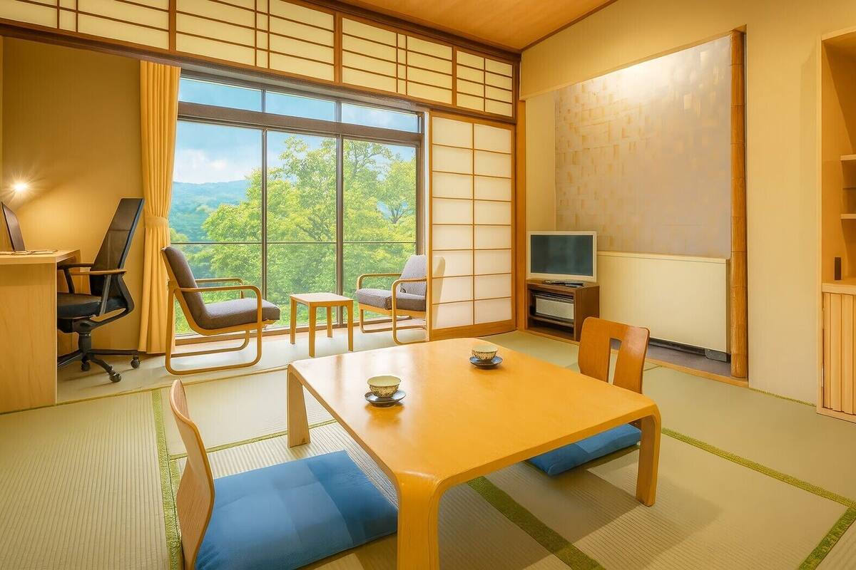 Ein traditioneller japanischer Raum mit Tatami-Boden, einem niedrigen Tisch mit einer Schale, einem Fernseher und einem Bücherregal.