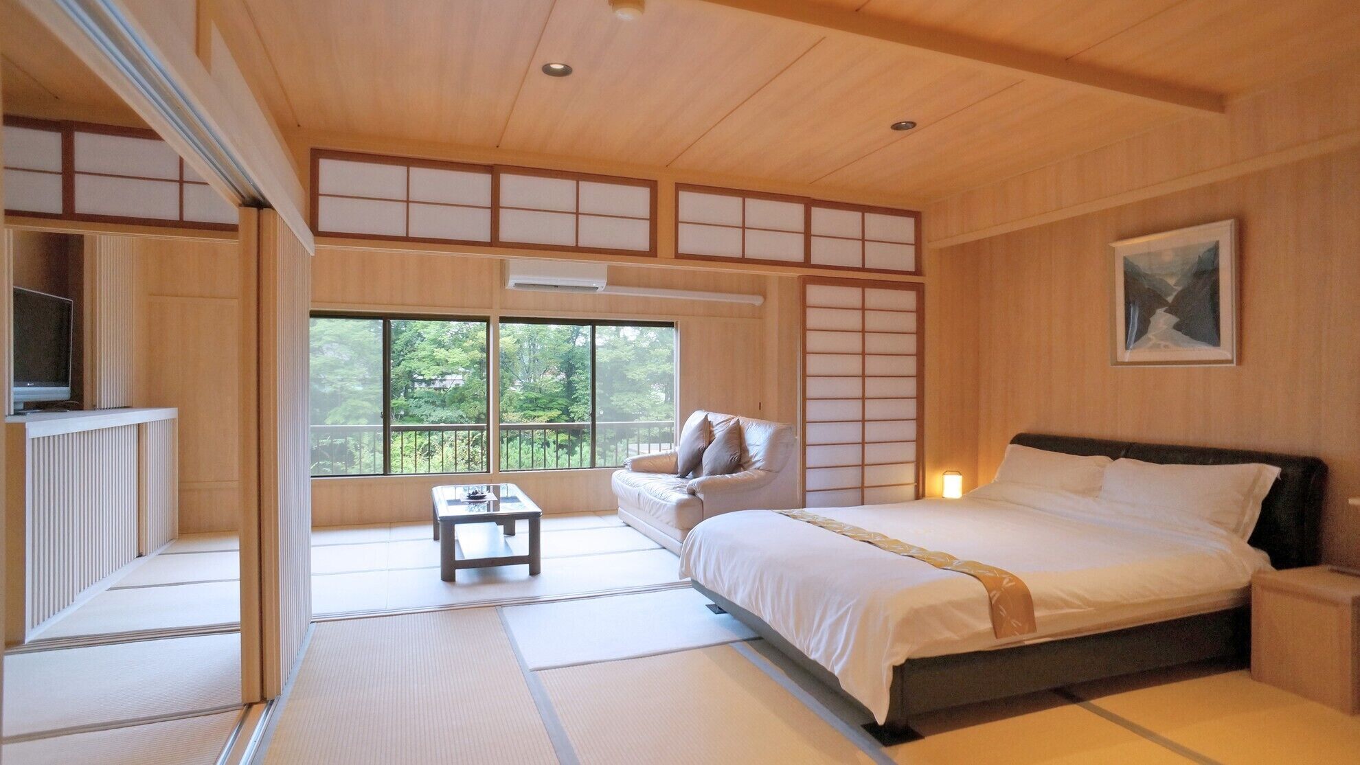 A traditional Japanese-style bedroom with tatami flooring, a bed, a sofa, and a television.