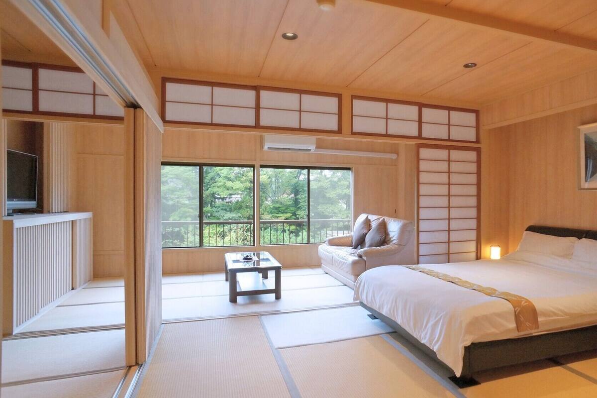 Ein traditionell gestaltetes japanisches Schlafzimmer mit Tatami-Böden, einem Bett, einer Couch und einem Fernseher.