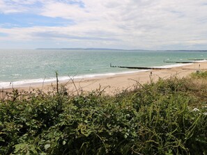 A beach with a wooden jetty extending into the sea, surrounded by dense greenery. - The Well House (Bournemouth)