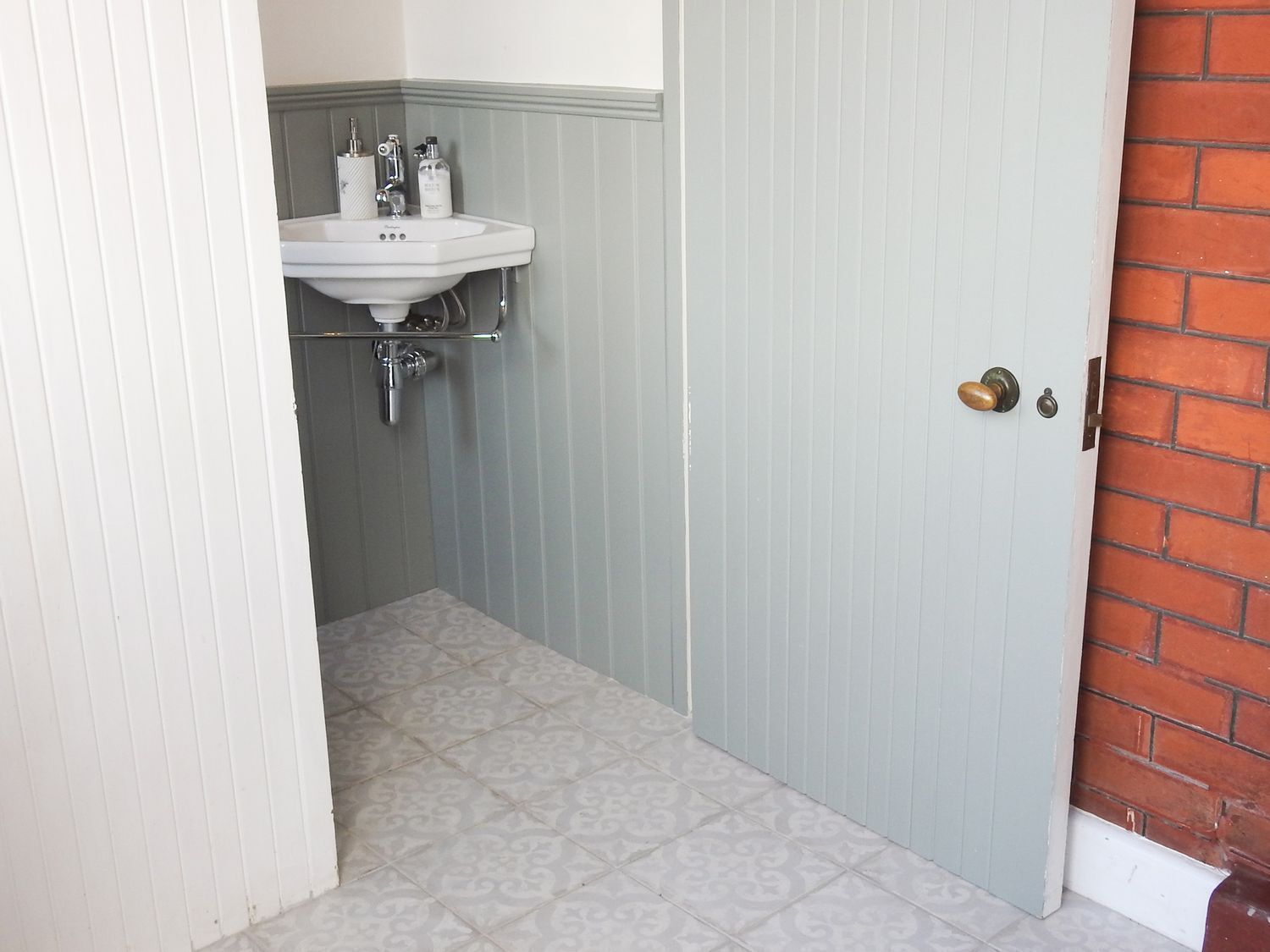 Un baño pequeño con un lavamanos blanco, un espejo y una puerta que da a un muro de ladrillo.