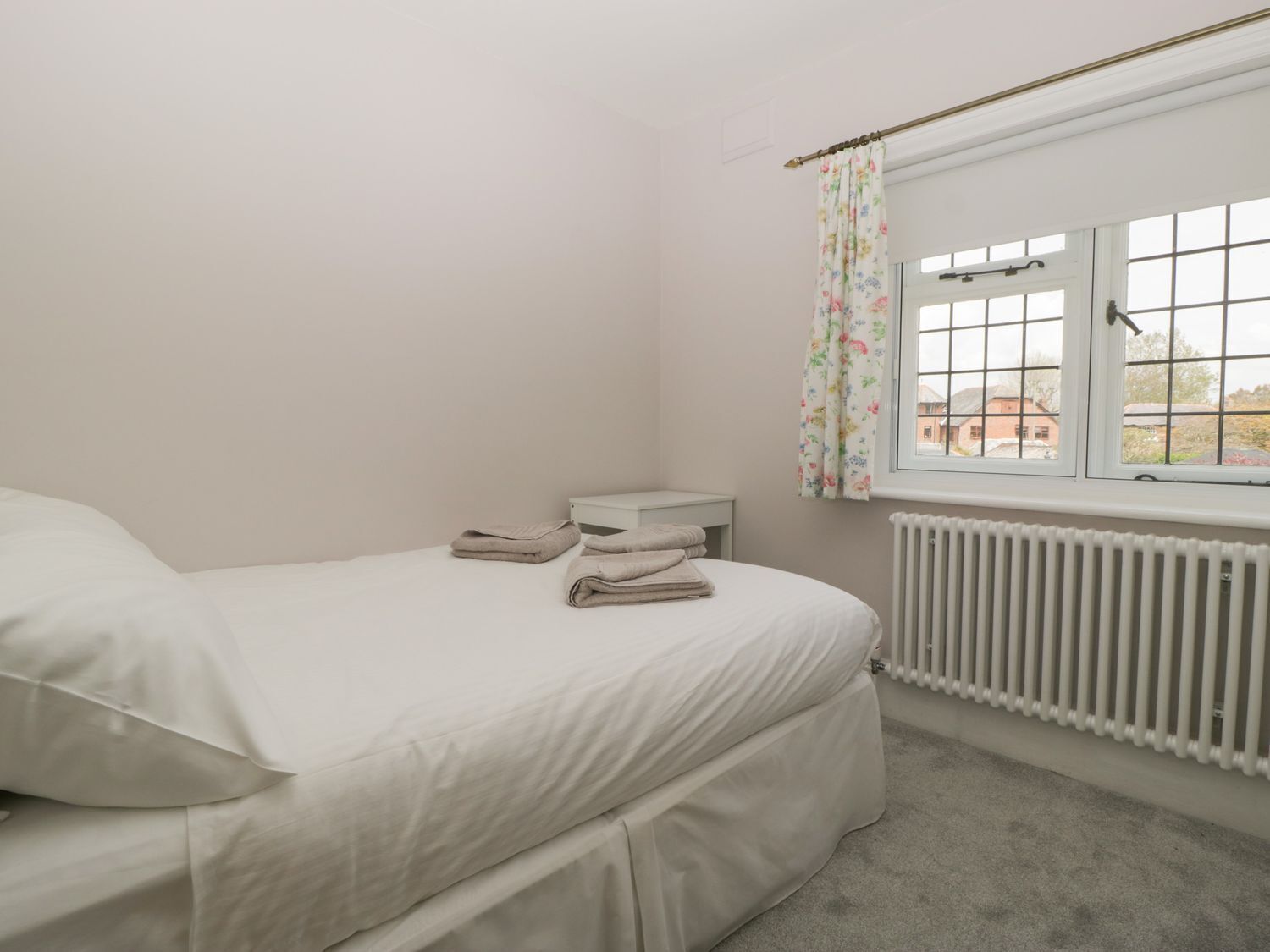 Ein Schlafzimmer mit einem Bett, einem Nachttisch, einem Fenster mit floralem Vorhang und einer Heizung.