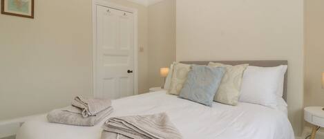 A neatly made bed with pillows and a folded towel, a white door, and a small bedside table with a lamp.