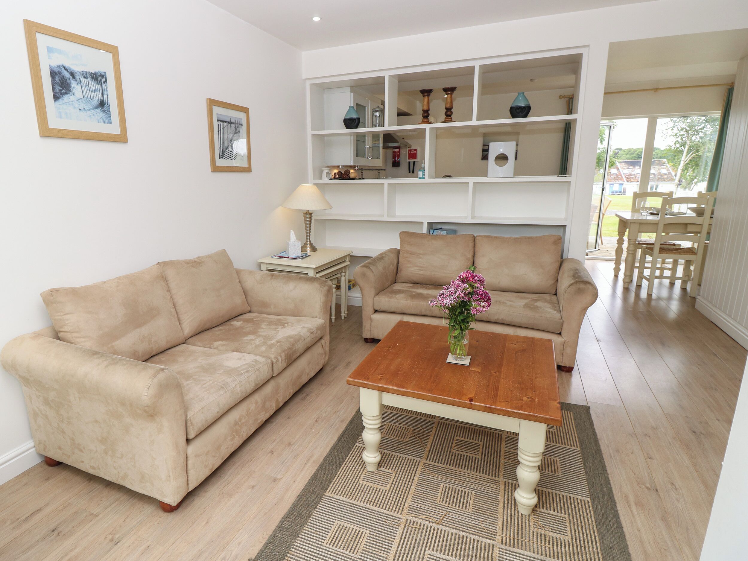 A living room with two beige sofas, a wooden coffee table with a vase of flowers, and a patterned rug.