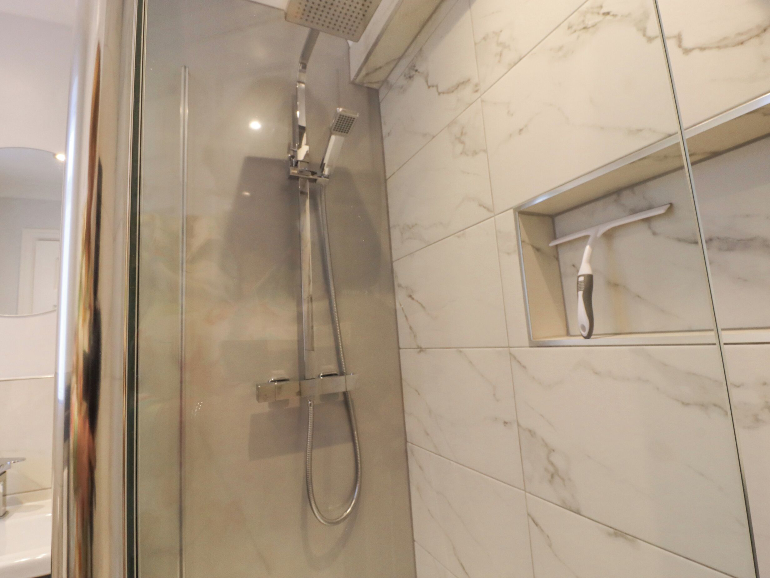Een moderne badkamer met een douche met glazen wand, marmeren tegels en een ingebouwde tandenborstelhouder.
