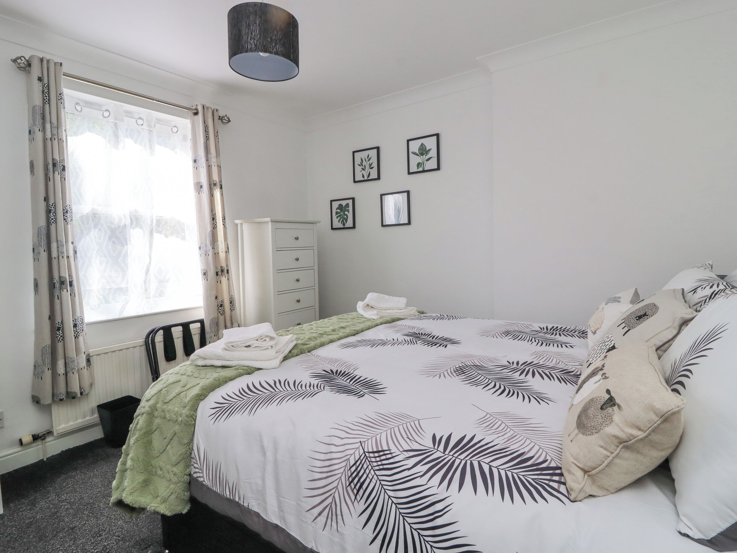 A bedroom with a bed, a dresser, a radiator, and a window with curtains.