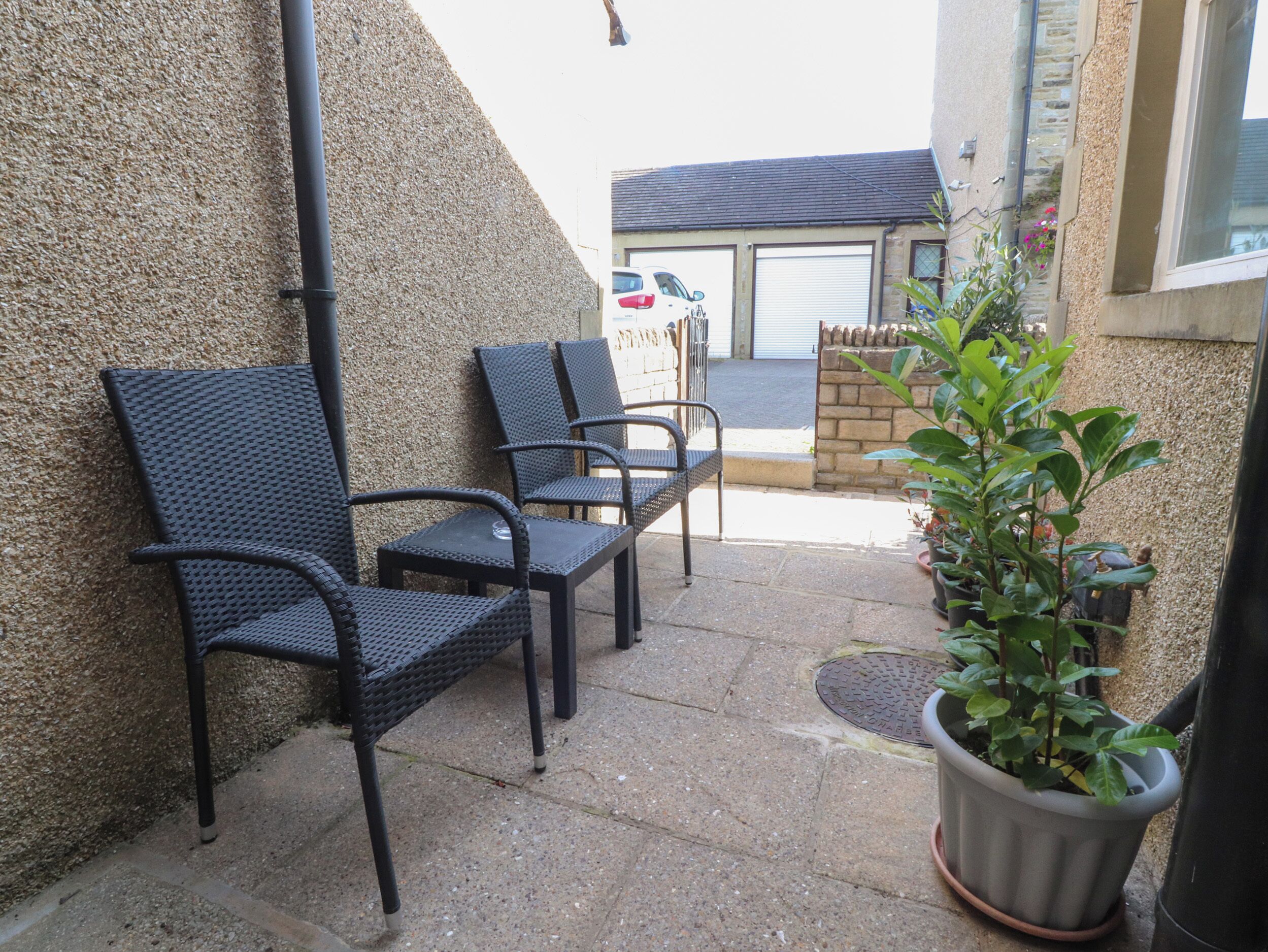 A patio with two black metal chairs and a potted plant.