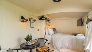 Ein gemütliches Zimmer mit einem Bett, einem kleinen Tisch mit einer Pflanze, einem Sessel und einem Fellteppich.