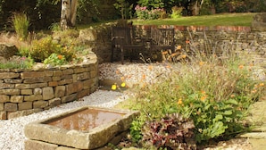 A garden with a stone wall, a wooden bench, and a small water feature.