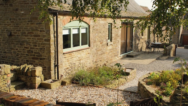 A stone building with a gravel pathway, a wooden bench, and a table with chairs outside.