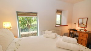 A bedroom with a large bed, a desk, a chair, a radiator, and a window with a view of greenery.