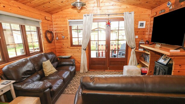 A cozy cabin interior with a leather sofa, a television, and a bookshelf. - Touchwood Lodge (Narberth)