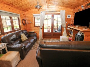 Un intérieur de chalet chaleureux avec un canapé en cuir, un téléviseur et une bibliothèque.