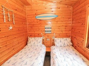 A cabin with two beds, wooden walls, a surfboard decoration, and a beach-themed sign. - Touchwood Lodge (Narberth)