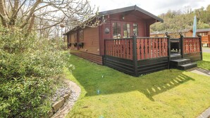 A wooden cabin with a fenced porch and a small deck. - Touchwood Lodge (Narberth)