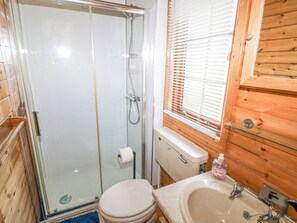A bathroom with a glass-enclosed shower, a toilet, a sink with a glass shelf, and wooden paneling. - Touchwood Lodge (Narberth)