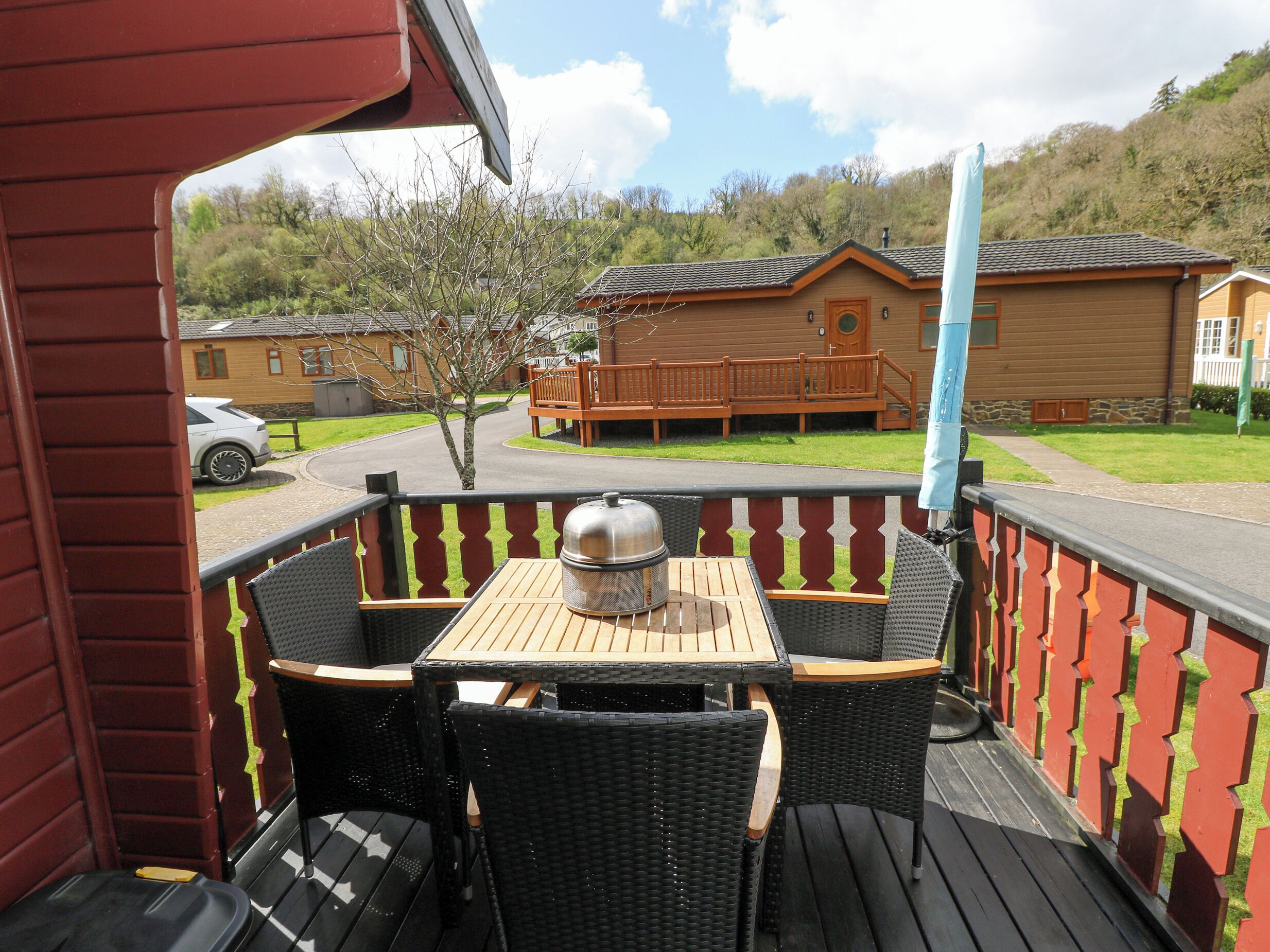 A wooden deck with a table and chairs, overlooking a residential area with houses and a parked car.