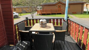 A wooden deck with a table and chairs, overlooking a residential area with houses and a parked car. - Touchwood Lodge (Narberth)