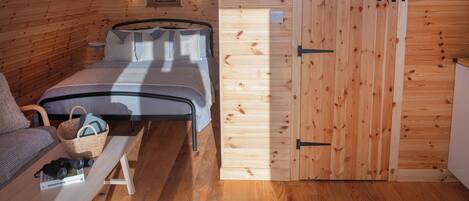 A cozy wooden cabin room with a bed, a bench, and a door.